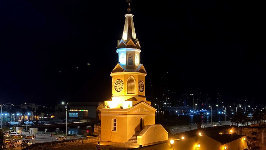 The iconic Clock Tower of Cartagena, Colombia, brightly illuminated at night against a dark sky, with city lights twinkling in the background.