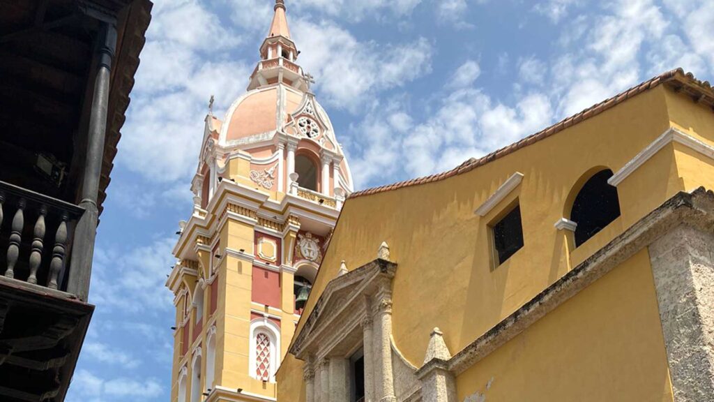 Historic yellow and red church dome with a clock tower and colonial architecture under a bright sky in Cartagena, Colombia.
