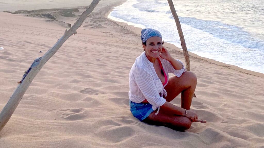 Paola Yepes sitting on the immense sand dunes of La Dunas de Taroa in La Guajira, Colombia, with the ocean visible in the background.