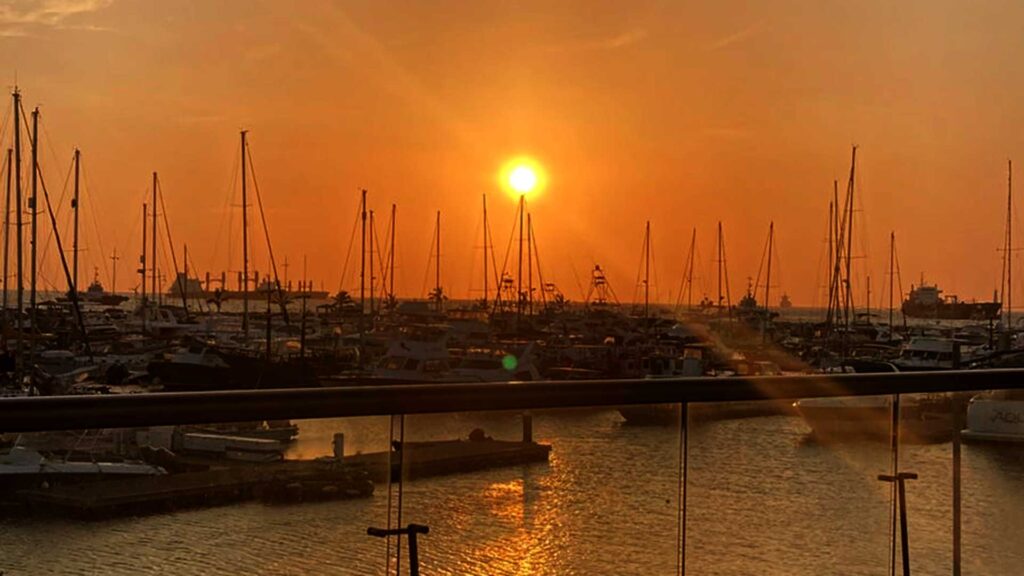 Vibrant orange sunset over the Santa Marta Marina in Colombia, with numerous sailboats and yachts silhouetted against the glowing sky and shimmering water