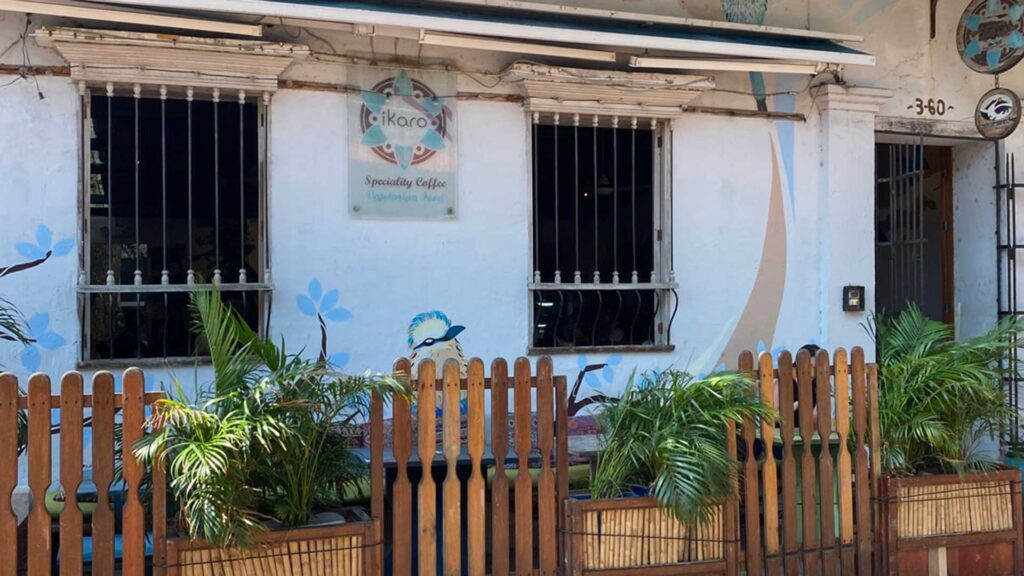 Exterior of "Ikaro" specialty coffee and vegetarian food cafe with a mural and wooden fence in the historic center of Santa Marta, Colombia.