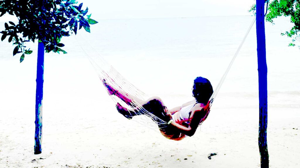 Person relaxing in a hammock between two trees on a white sandy beach with calm ocean in the background, Isla Palma, San Bernardo, Colombia.