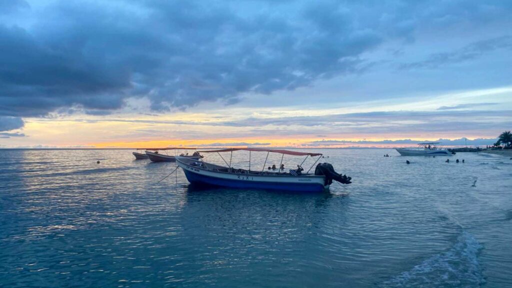 Small boats anchored in clear, calm ocean water at Playa Salguero, Santa Marta, Colombia, with a colorful sunset sky of orange, pink, and blue.